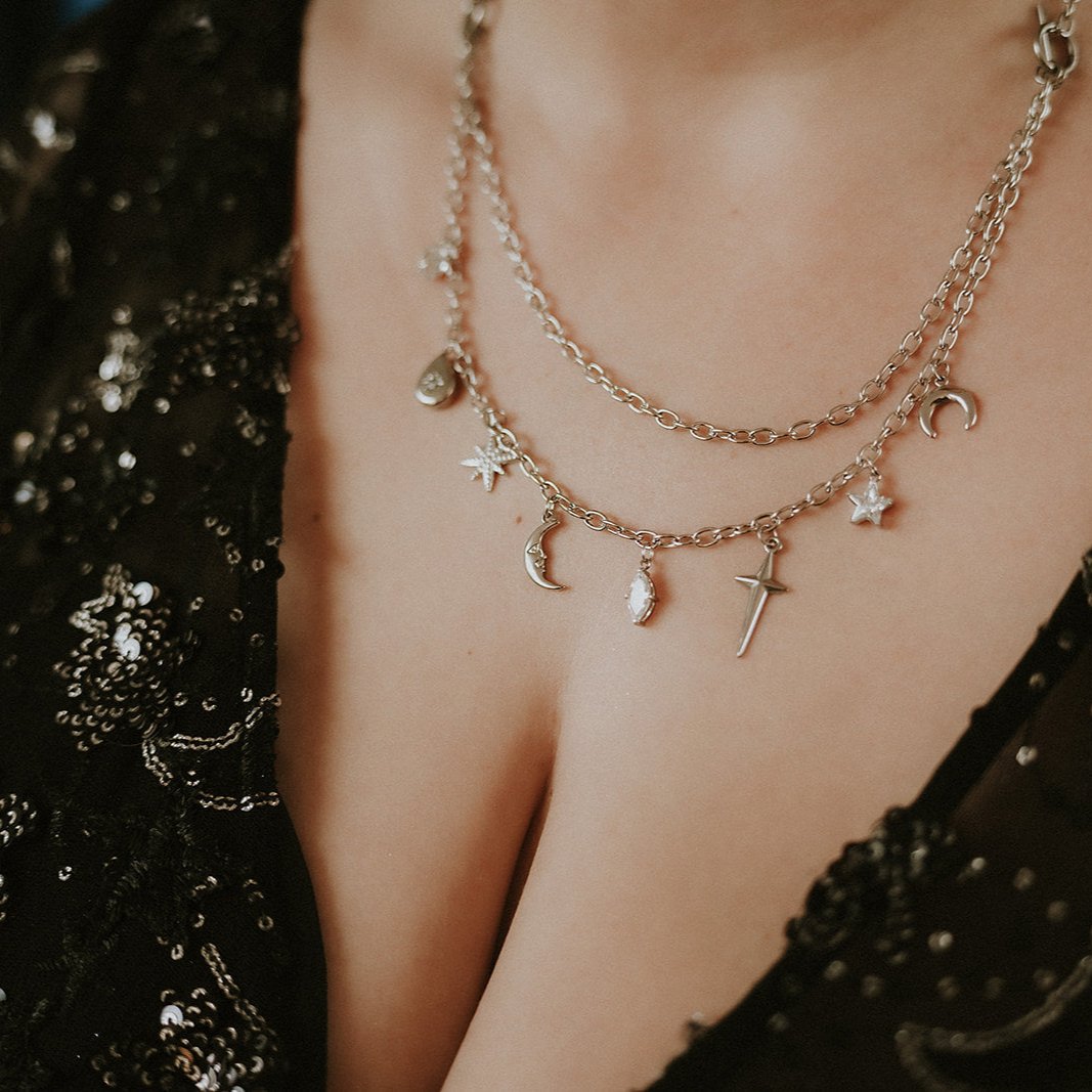 Layered necklaces with charms on a person wearing a black embellished garment.