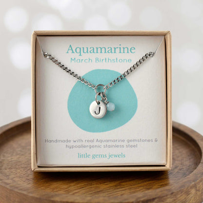 Aquamarine March Birthstone necklace with hand stamped initial inside an eco-friendly gift box sitting on wooden coaster