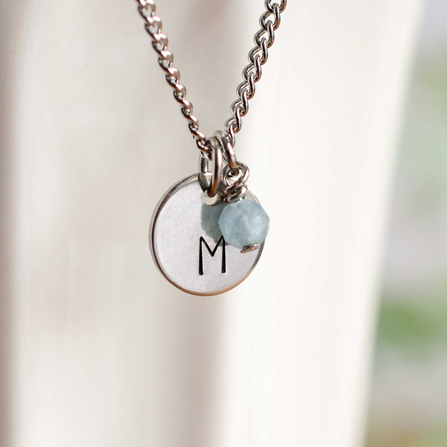 Close up of initial M letter pendant with Aquamarine March birthstone charm