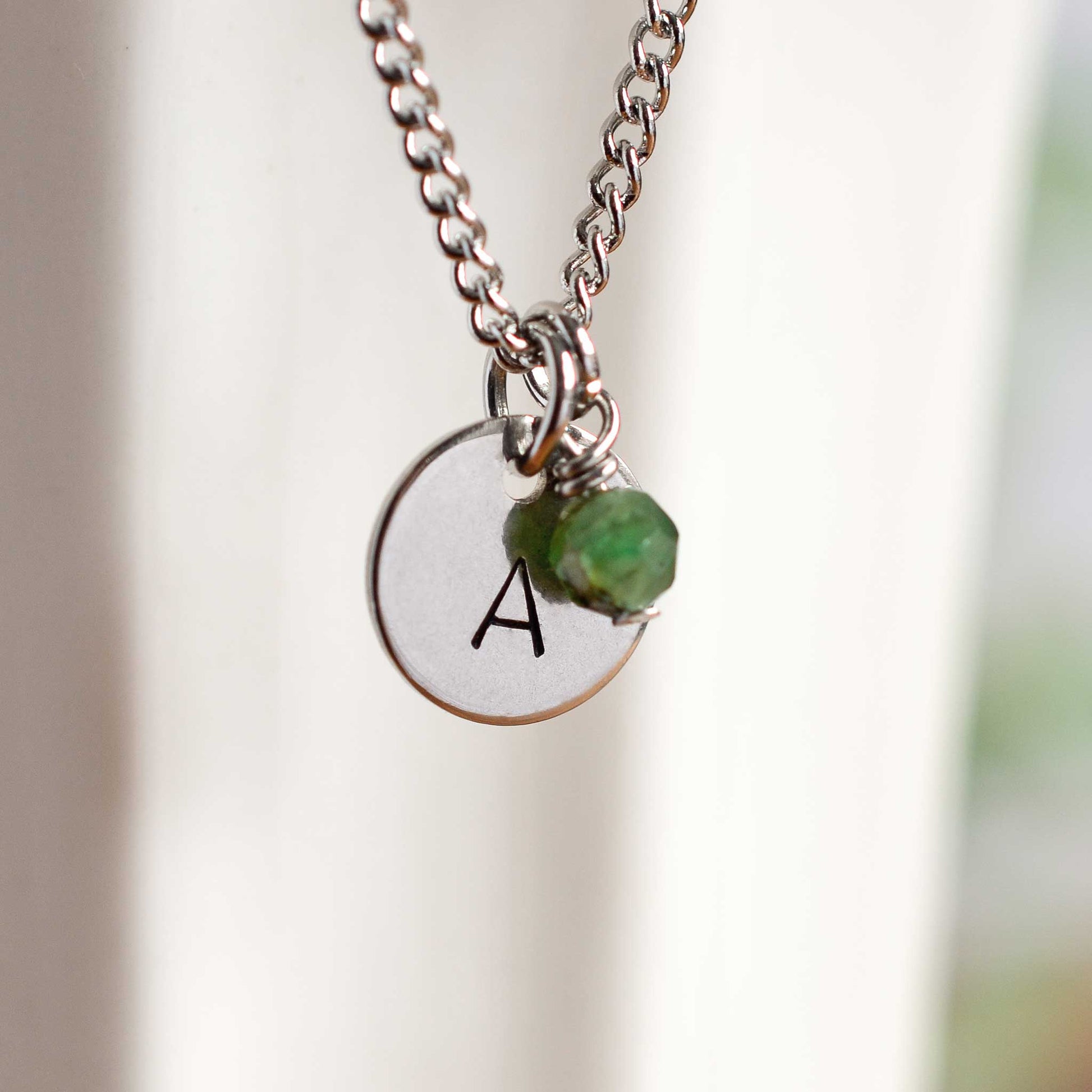 Close up of letter A disc initial pendant with Emerald May birthstone charm