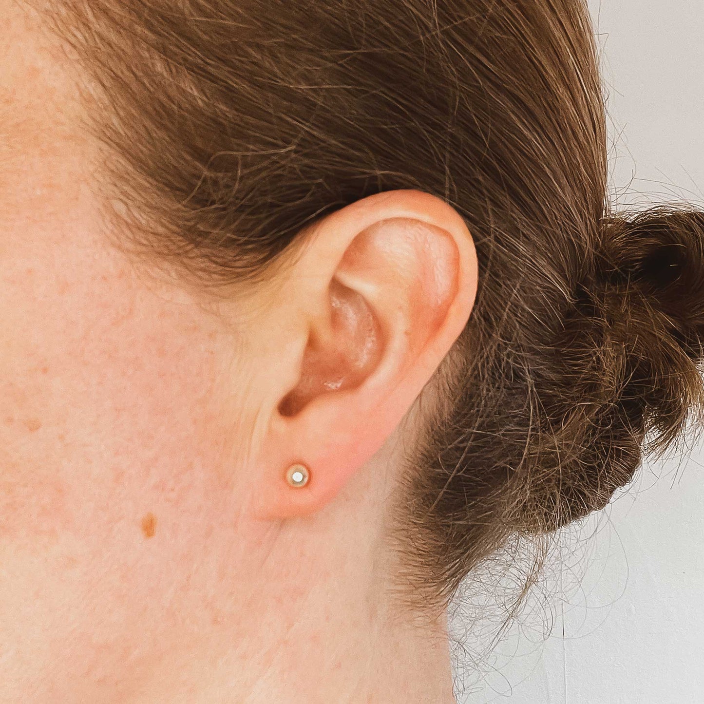Woman wearing tiny cream faux pearl stud earring in earlobe
