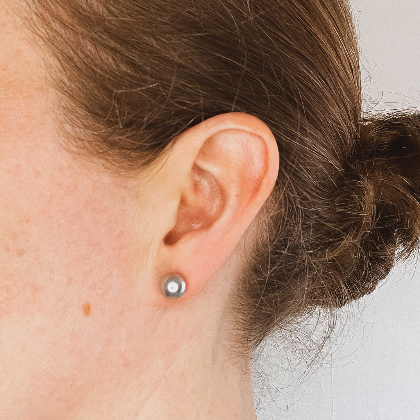 Woman wearing 8mm light grey faux pearl stud earring in earlobe