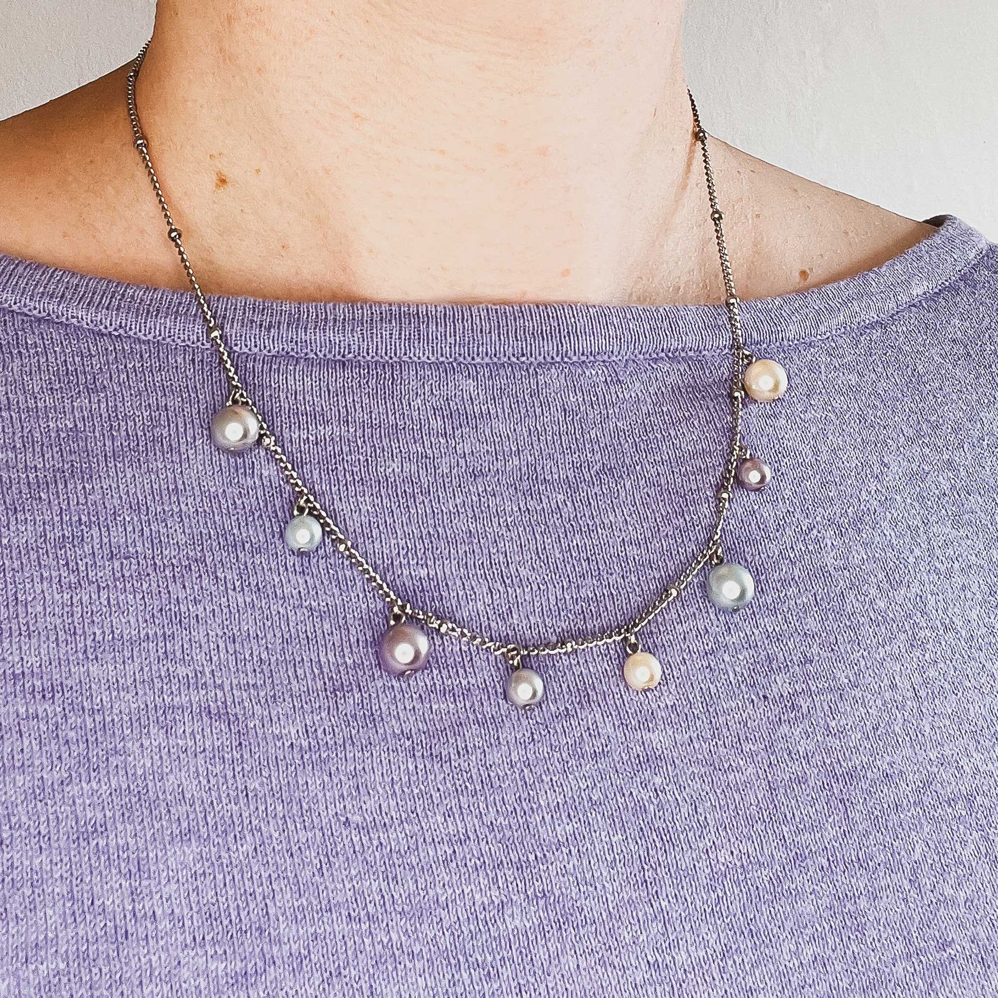 Woman wearing purple jumper and faux pearl charms necklace