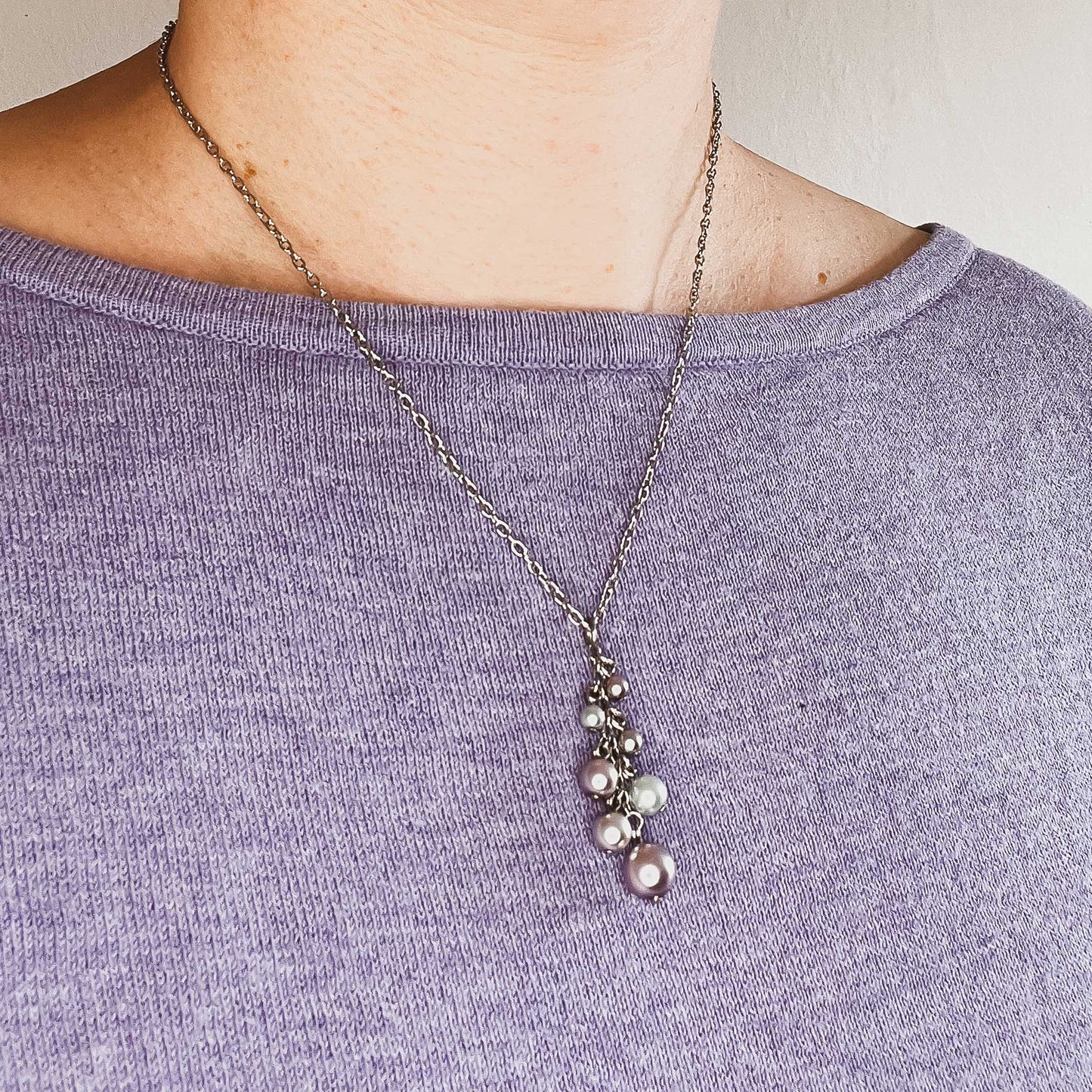 Woman wearing purple jumper and faux pearl cluster necklace