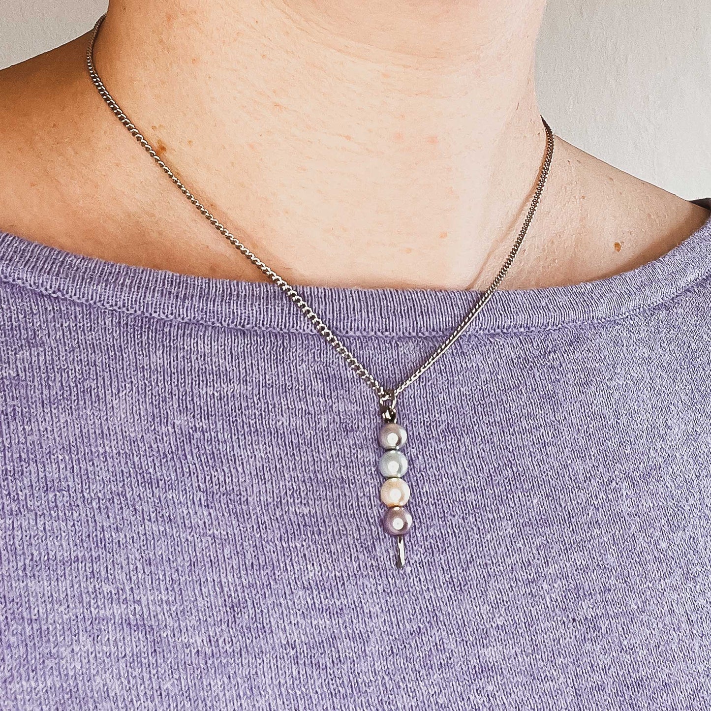 Woman wearing purple jumper and faux pearl stack pendant
