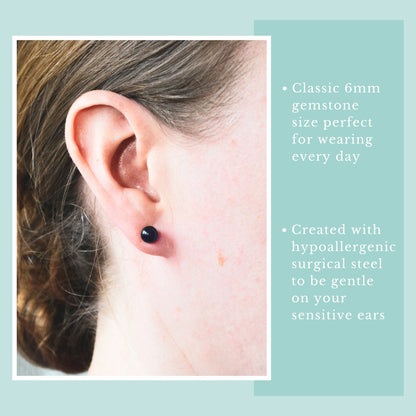 Close-up of a woman wearing a drak purple gemstone earring in earlobe.