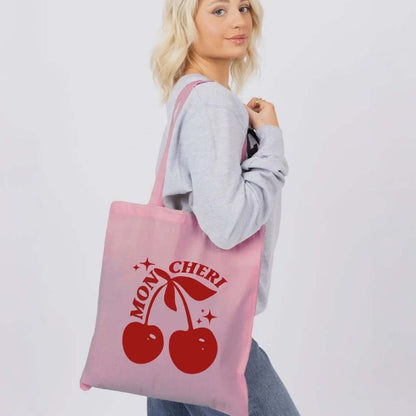 Person holding a pink tote bag with red cherries and text on a white background