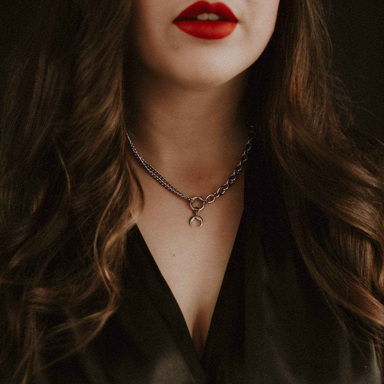 Close-up of a person wearing a chain necklace with a moon pendant, against a dark background.