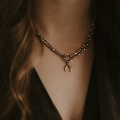 Close-up of a person wearing a chain necklace with a moon pendant.