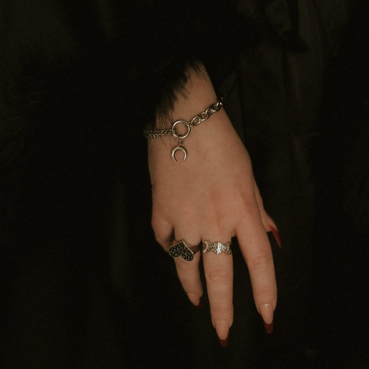 Hand wearing a bracelet and rings on a dark background