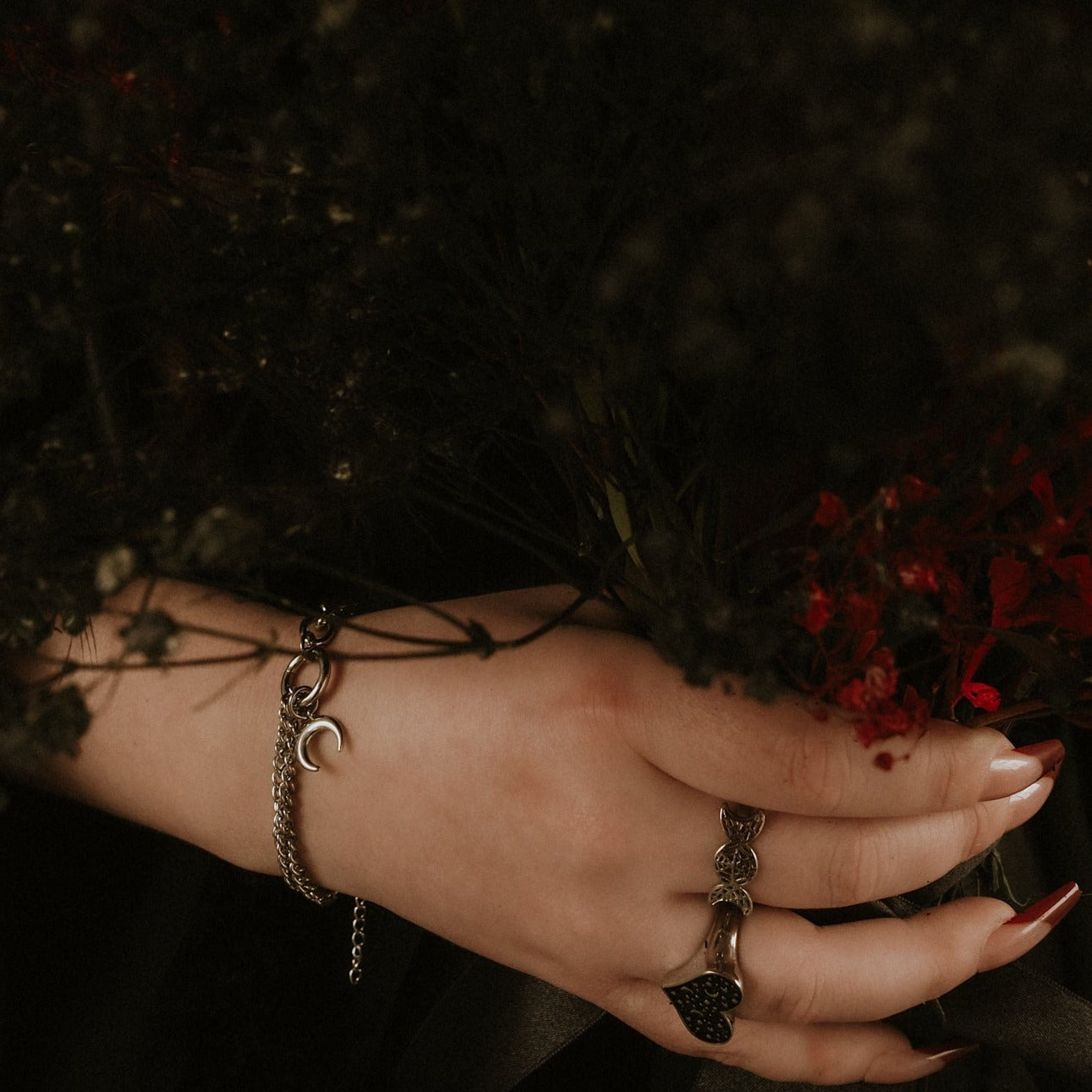 Hand wearing a bracelet and ring holding red flowers against a dark background