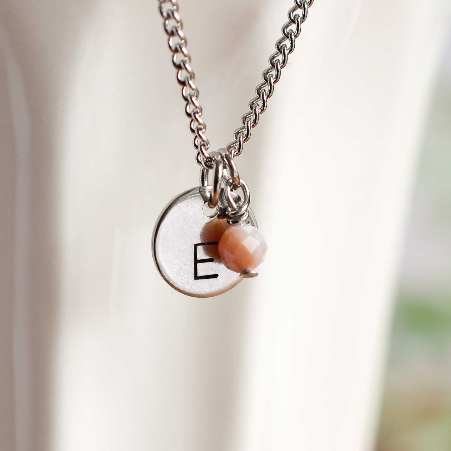 Close up of letter E disc initial pendant with Pink Opal October birthstone charm