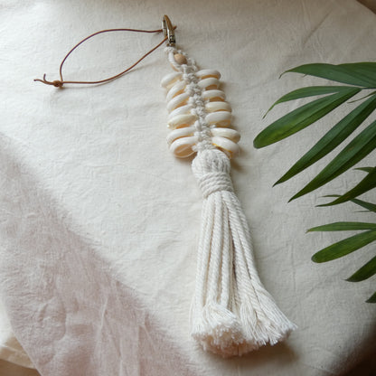 Decorative shell bag charm with tassel on a white fabric background