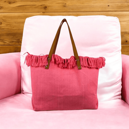 Pink tote bag with brown handles on a pink cushioned chair against a wooden wall.