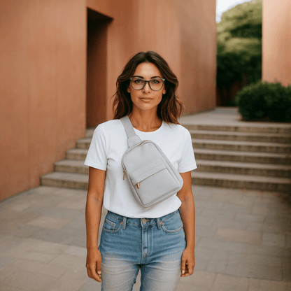 Woman wearing a white t-shirt, blue jeans, and a gray crossbody bag standing in front of a building with steps.