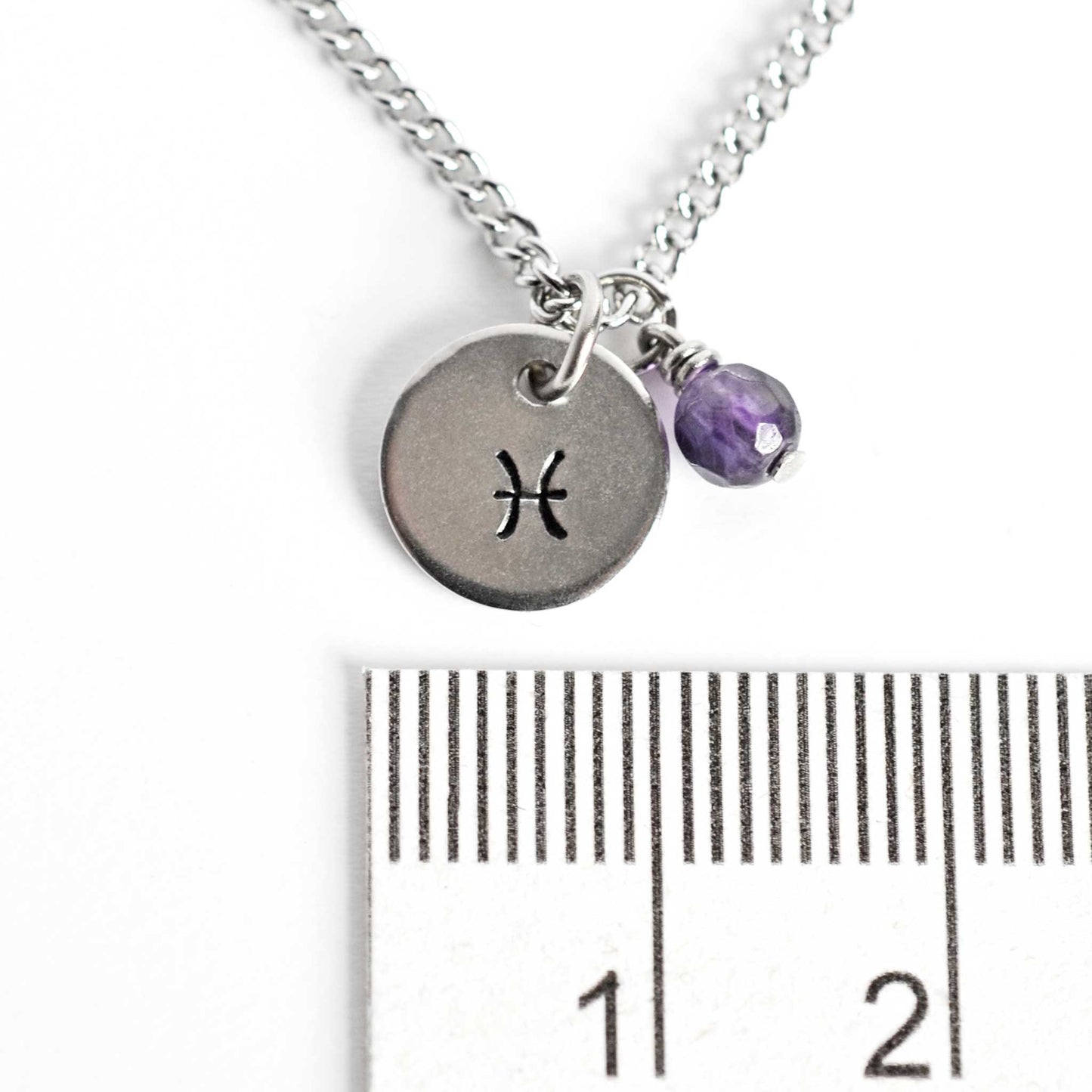 10mm round Pisces zodiac sign necklace next to ruler