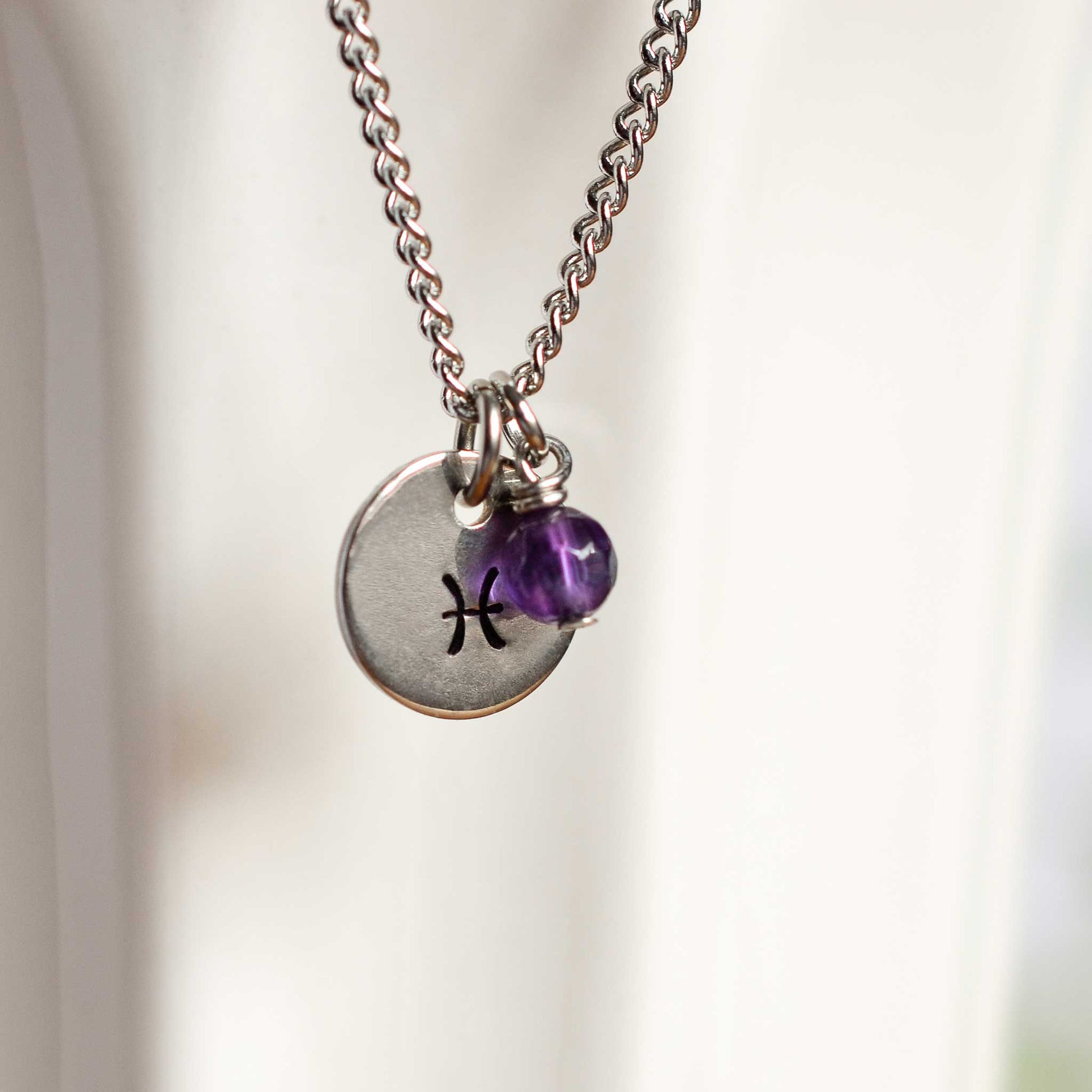 Close up of Pisces zodiac sign necklace with Amethyst gemstone charm on stainless steel chain