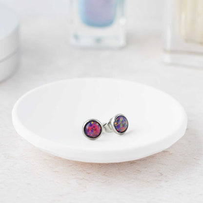 Purple round stud earrings on a white dish with a blurred background