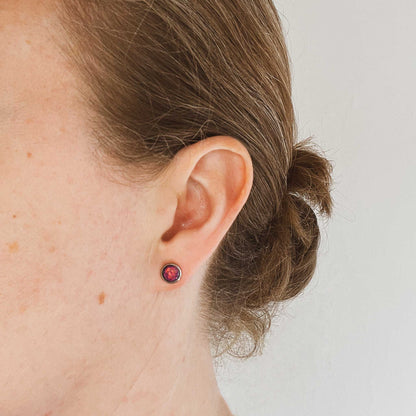 Close-up of an ear wearing a small purple earring with a plain background