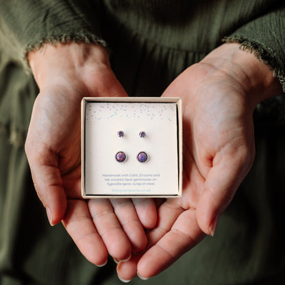 Hands holding a square gift box containing small and large purple stone stud earrings set.