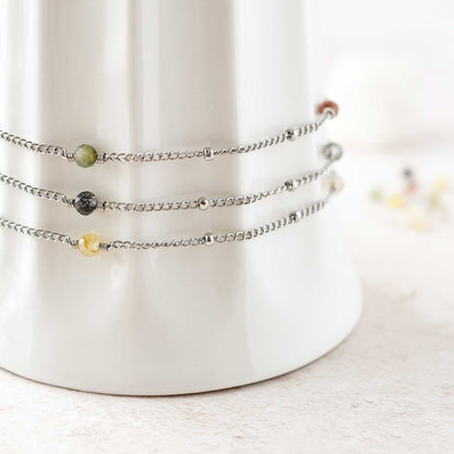 Three gemstone ankle bracelets stacked around a white cup.