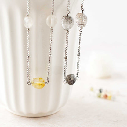 Close up of two Quartz gemstone necklaces hanging from white cup