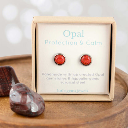 Red Opal earrings on a display card with 'Opal Protection & Calm' text, placed on a wooden surface.