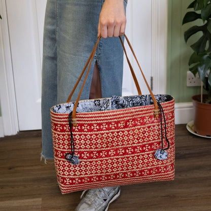 Person holding a red patterned tote bag with a plant in the background