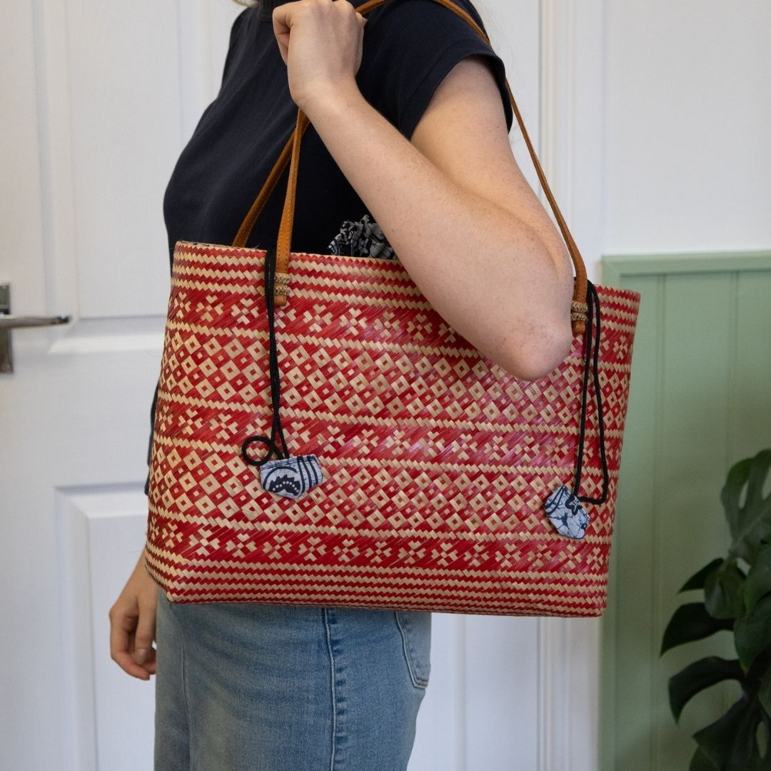 Person holding a red and beige patterned tote bag with a plant in the background