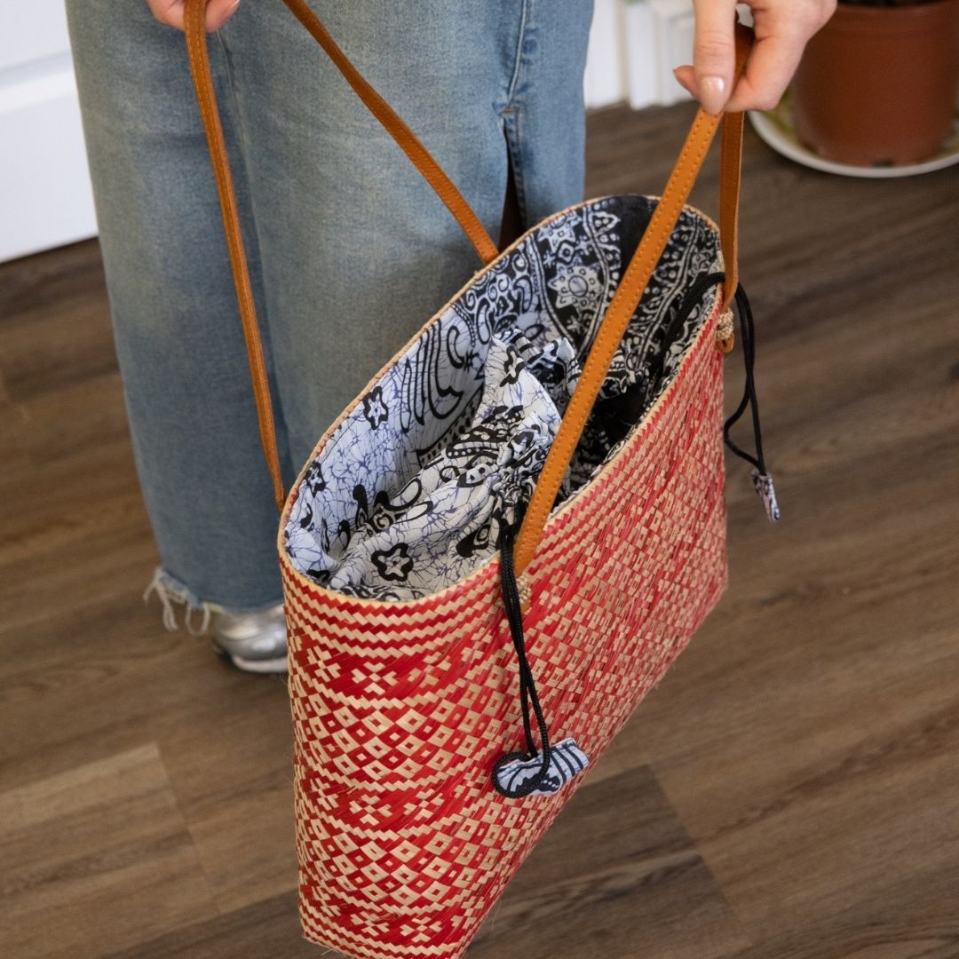 Person holding a red patterned bag with a brown strap on a wooden floor.