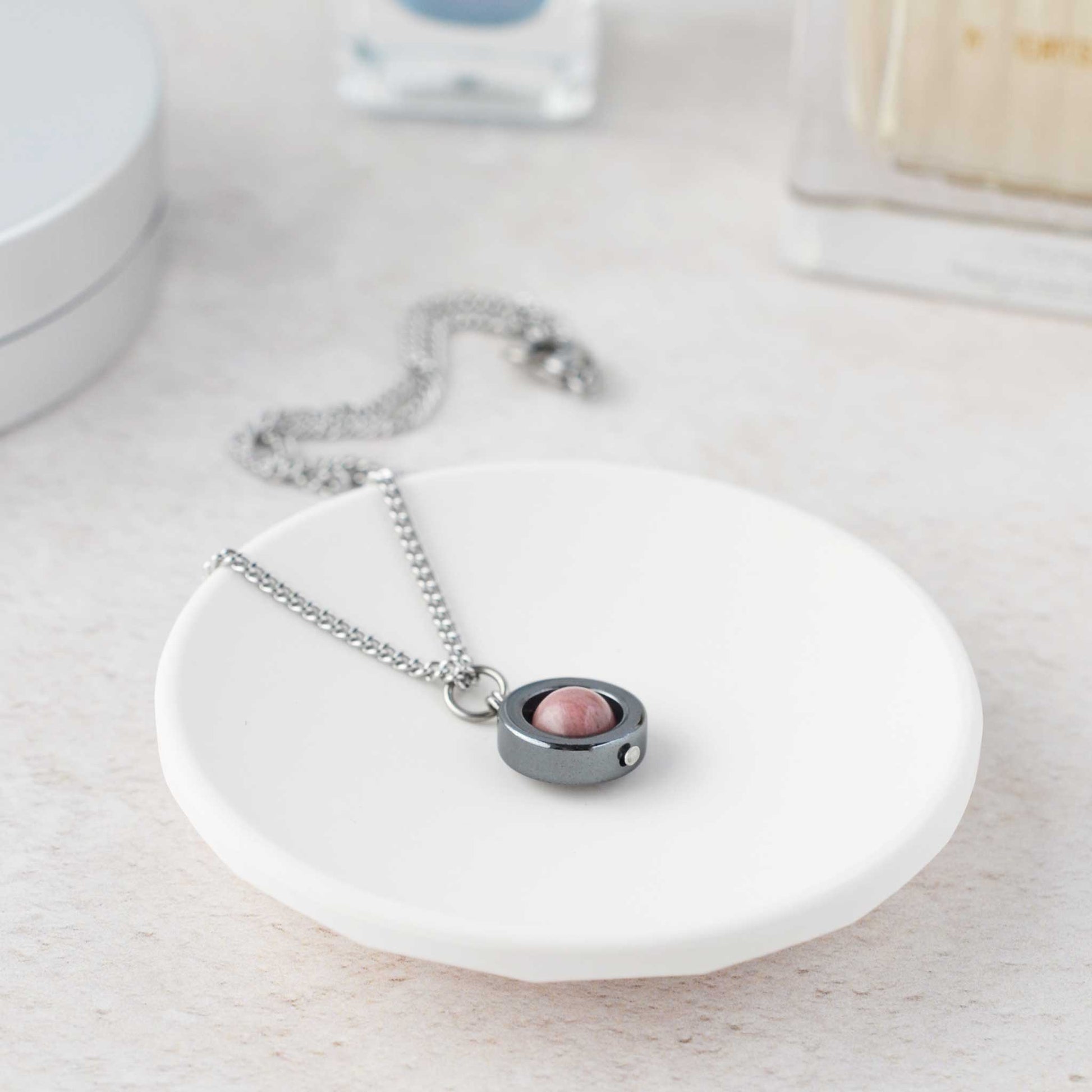 Rhodonite spinner necklace laying on white trinket dish.
