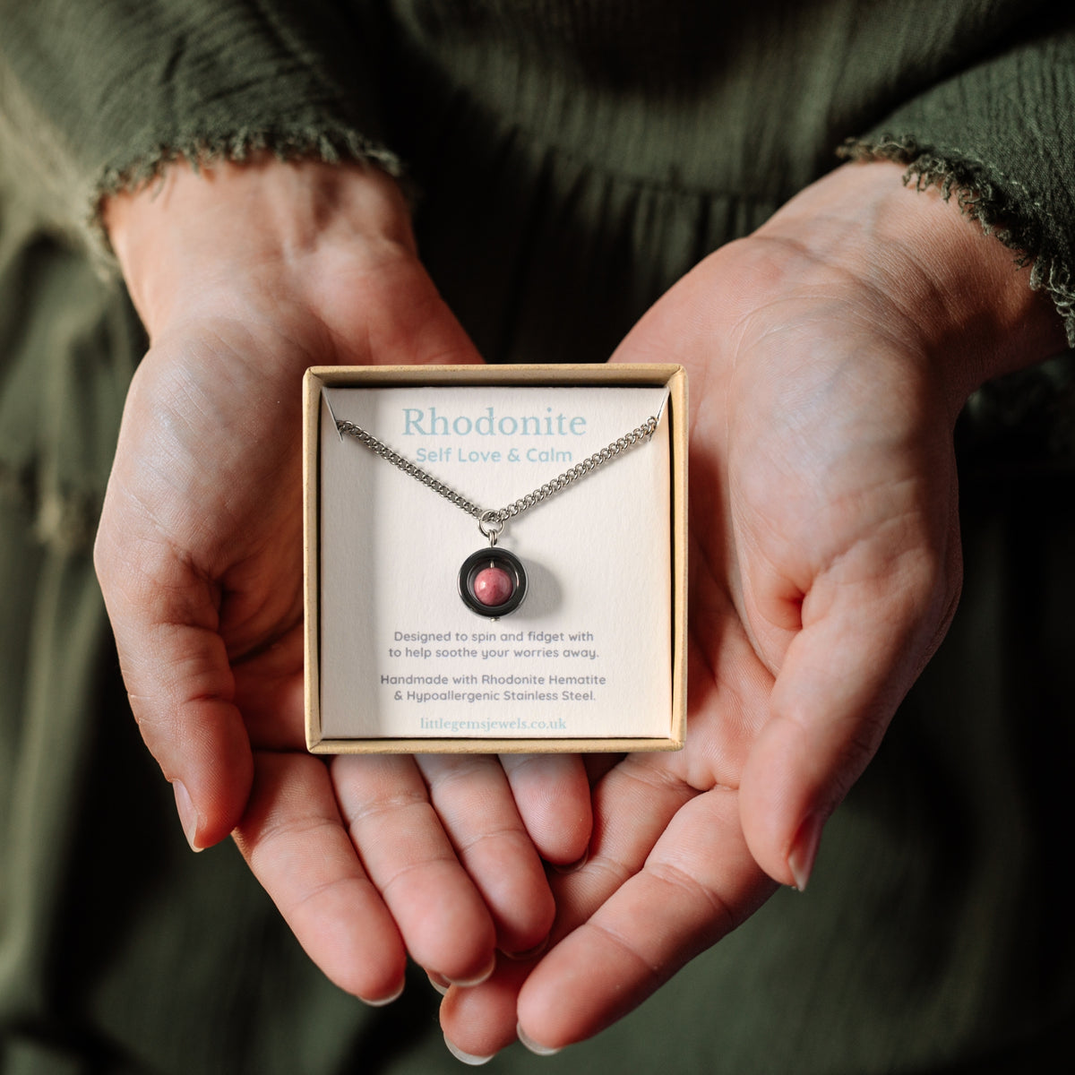 Rhodonite gemstone spinner necklace in a gift box being held in a woman's hands.