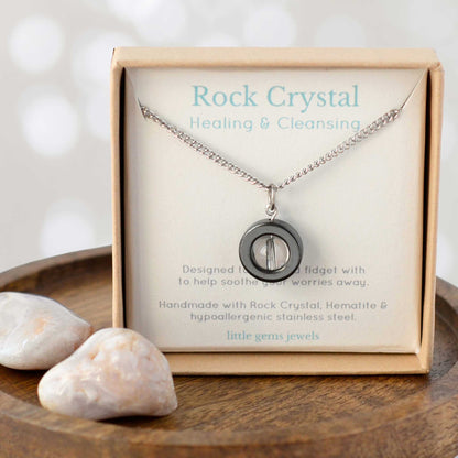 Necklace with pendant in a 'Rock Crystal Healing & Cleansing' box on a wooden surface with stones.