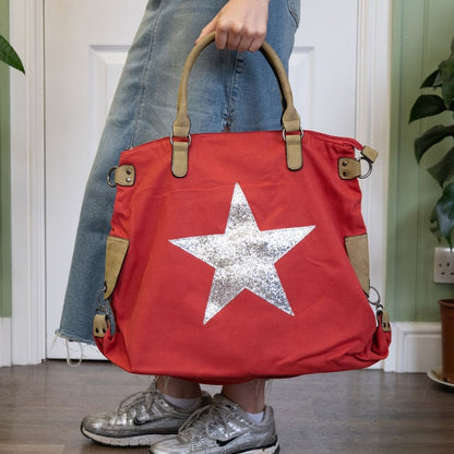Red bag with a silver star held by a person wearing jeans and silver shoes.