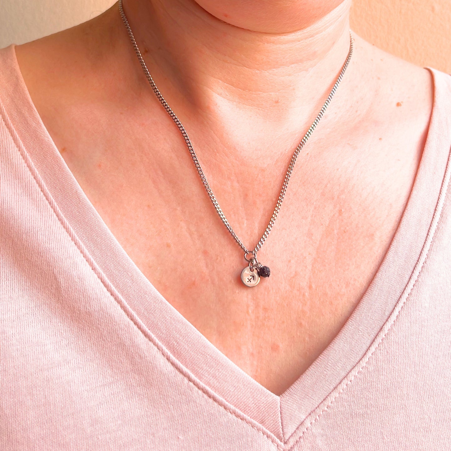 Woman wearing a pink v neck top and dainty Sagittarius zodiac sign necklace.
