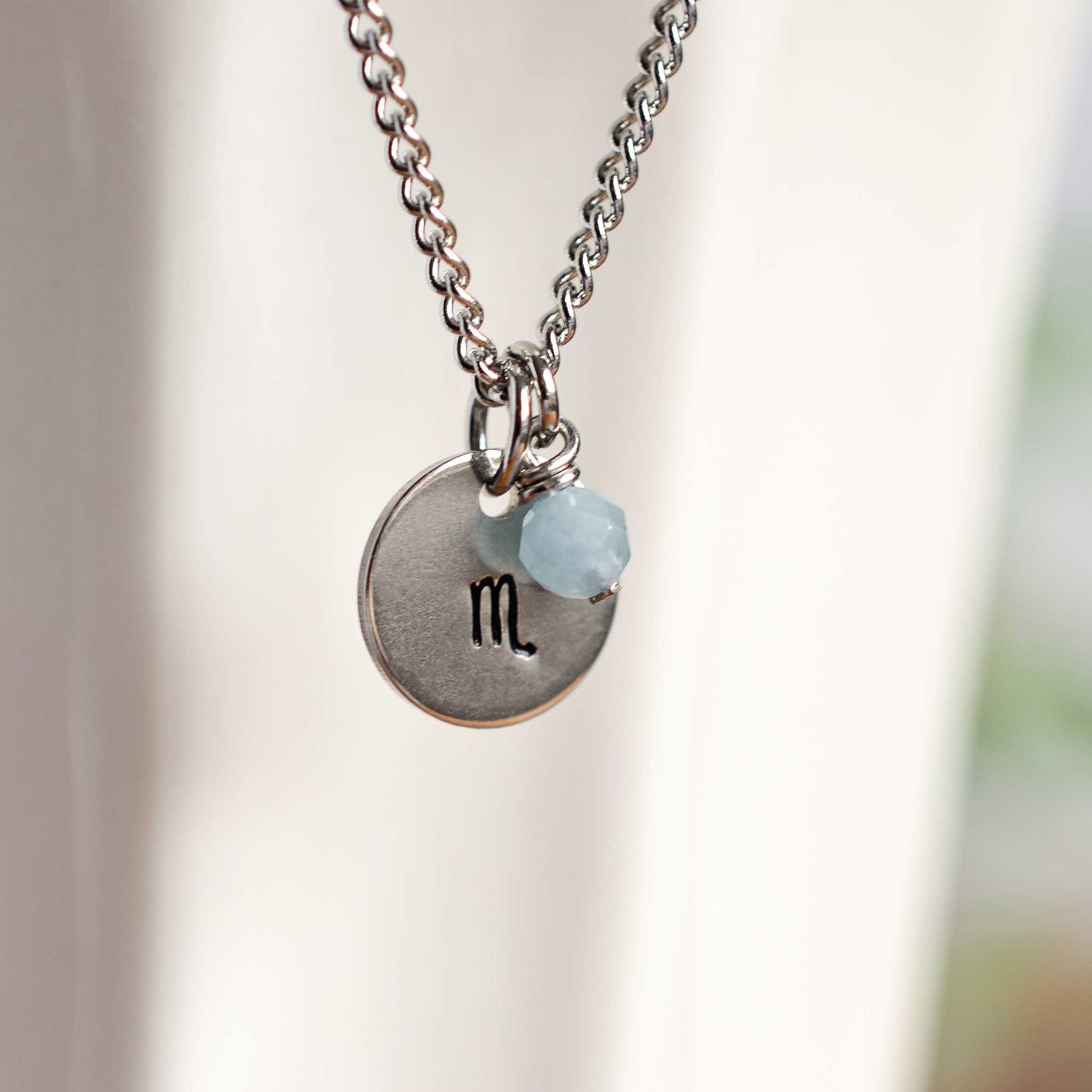 Close up of Scorpio zodiac sign necklace with Aquamarine gemstone charm on stainless steel chain