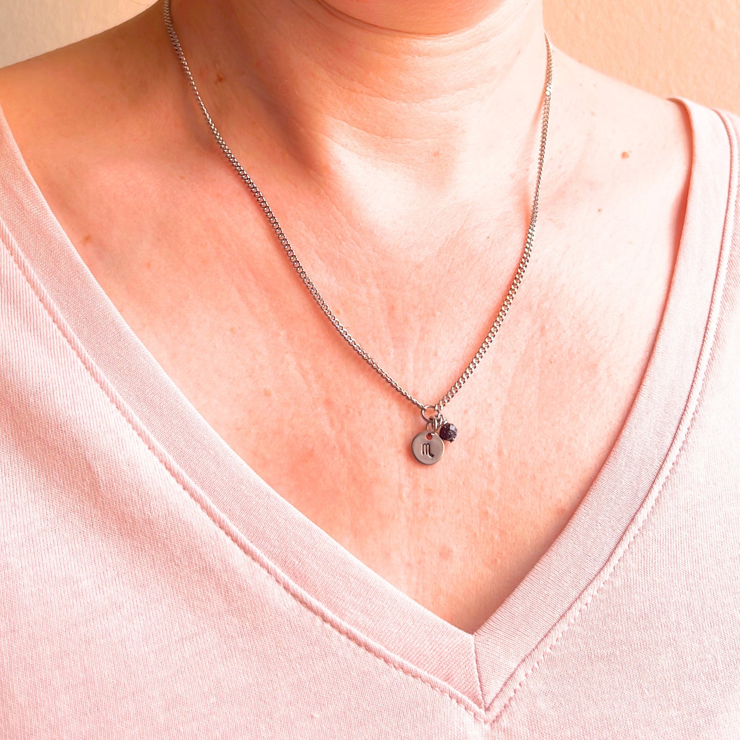 Woman wearing a pink v neck top and dainty Scorpio zodiac sign necklace.