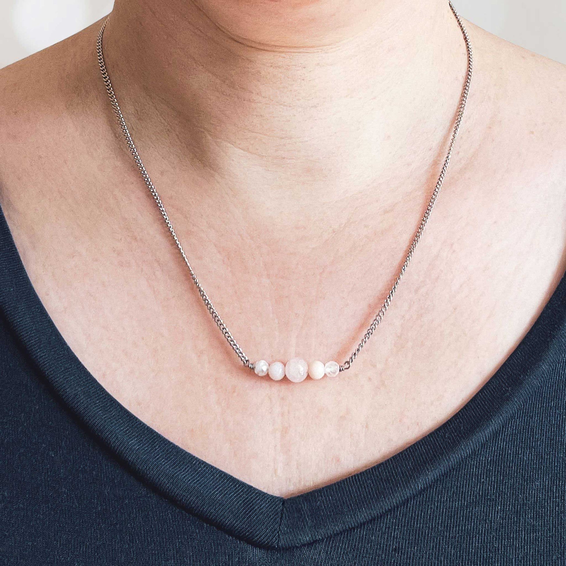 Woman wearing dark blue v neck top and dainty pale pink gemstone necklace
