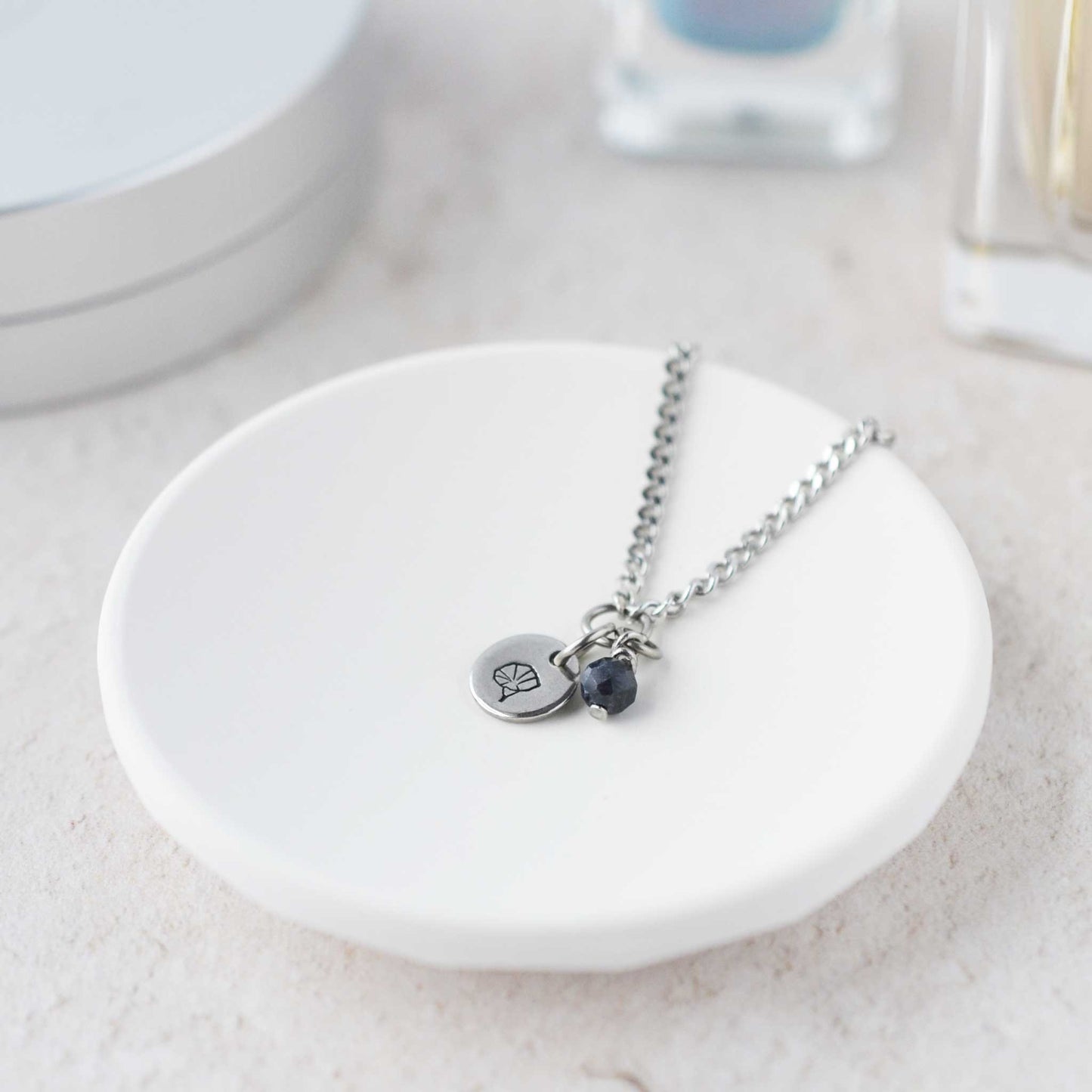 Tiny Morning Glory & Sapphire gemstone necklace laying in white trinket dish