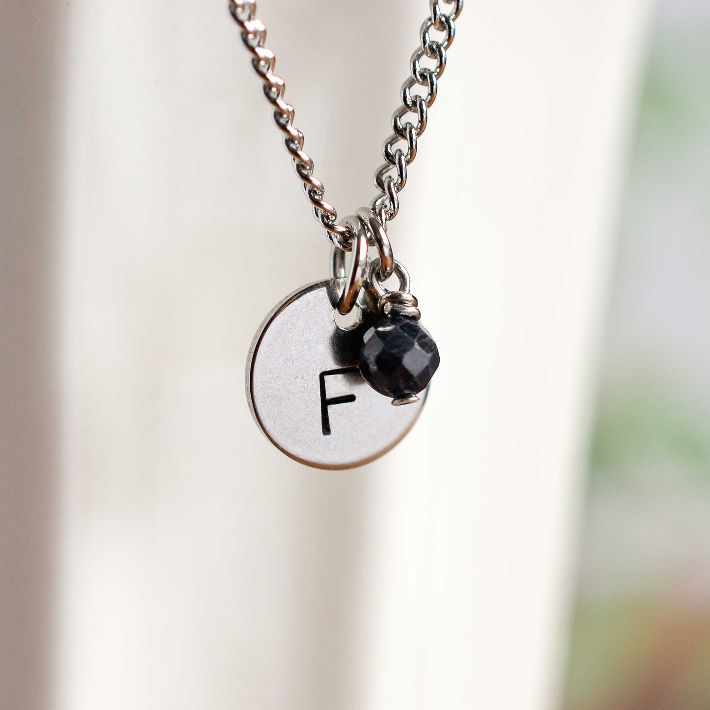 Close up of letter F disc initial pendant with Sapphire September birthstone charm