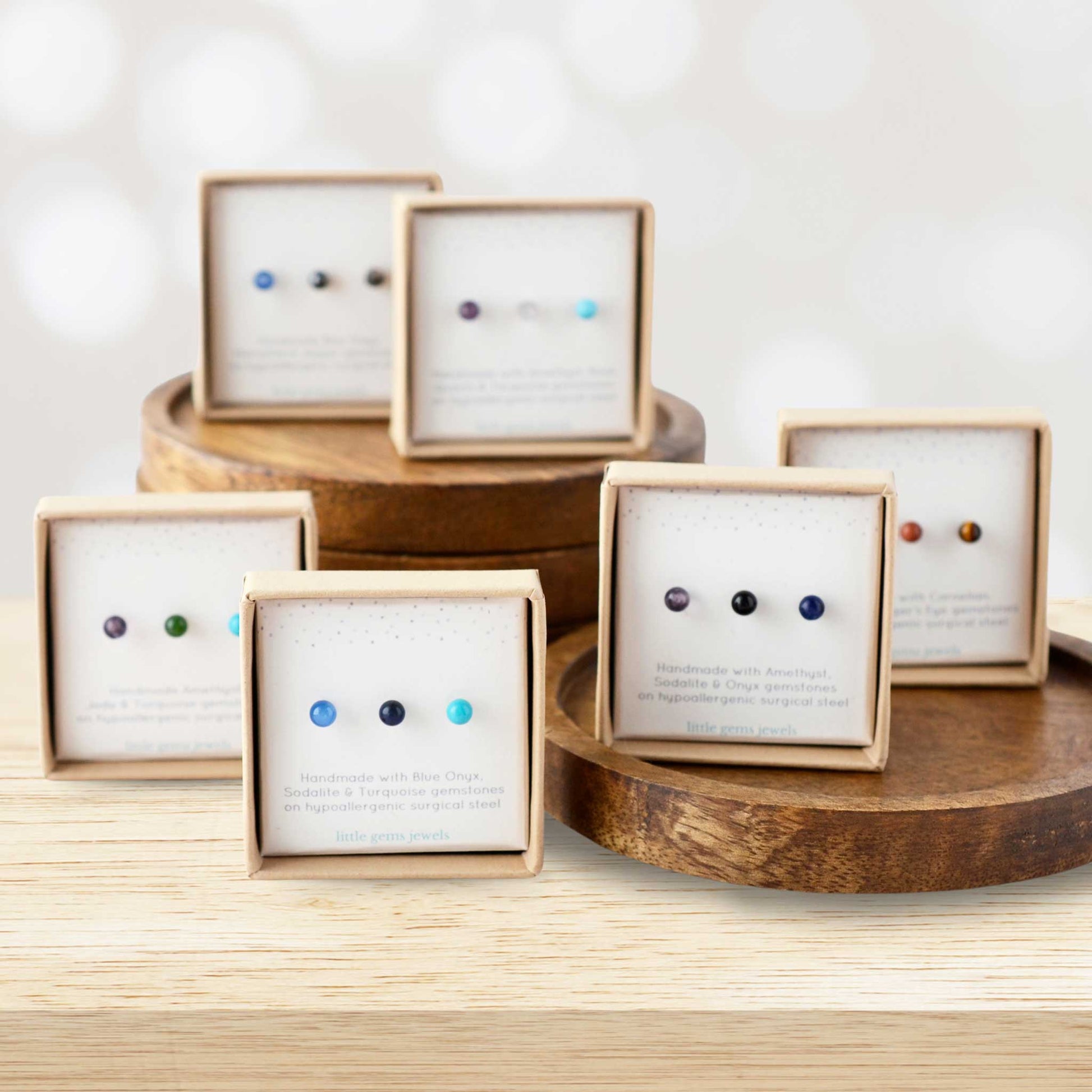 Gift sets of three single gemstone studs in eco friendly boxes stacked on wooden display.