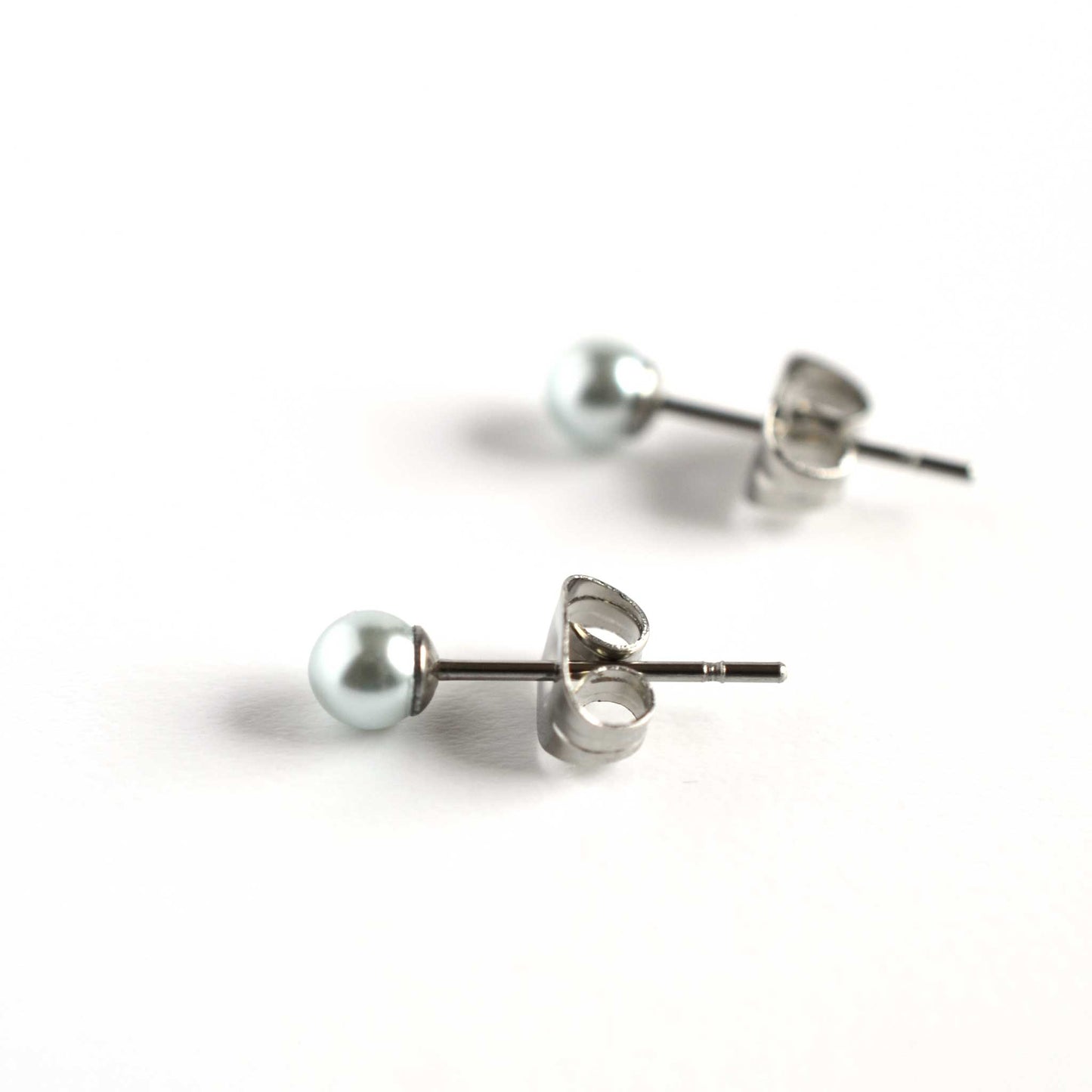 Side view of tiny pale blue faux pearl stud earrings on white background