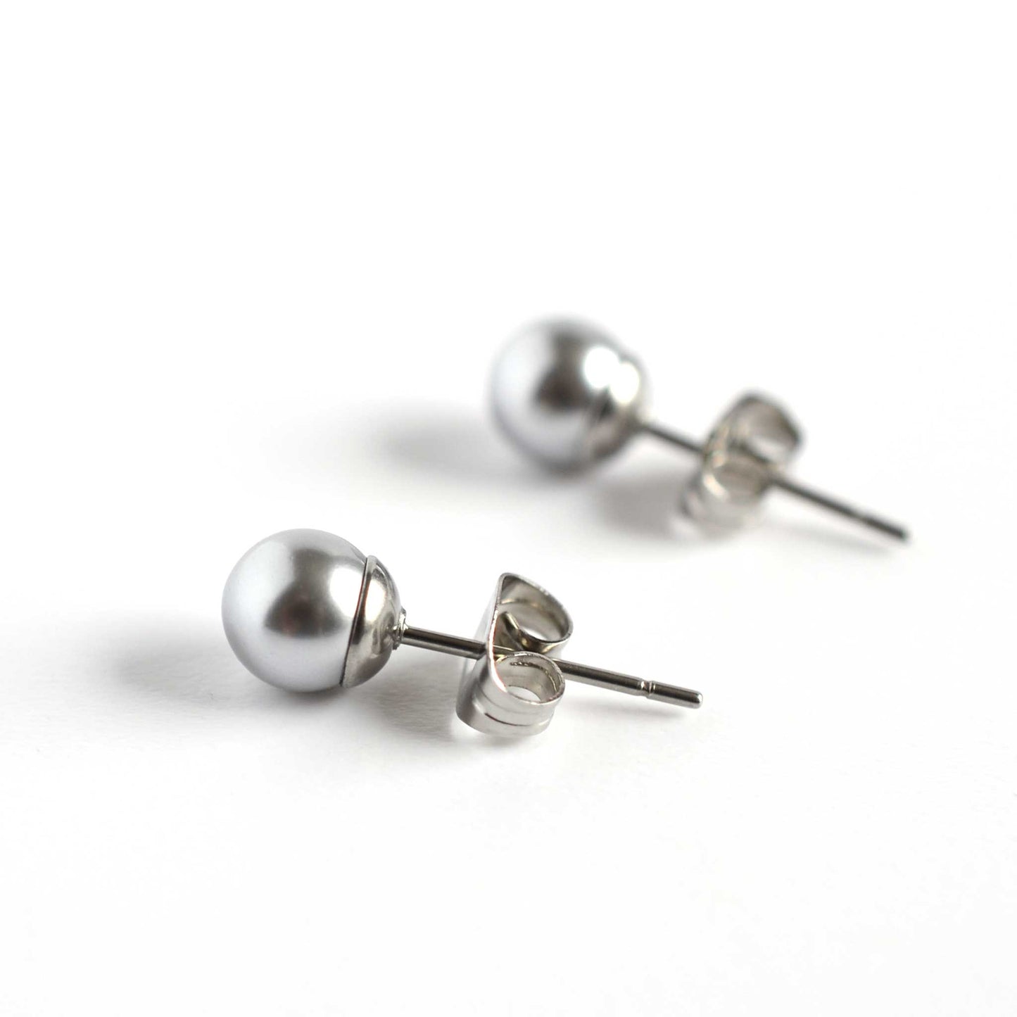 Side view of light grey 6mm faux pearl stud earrings on white background