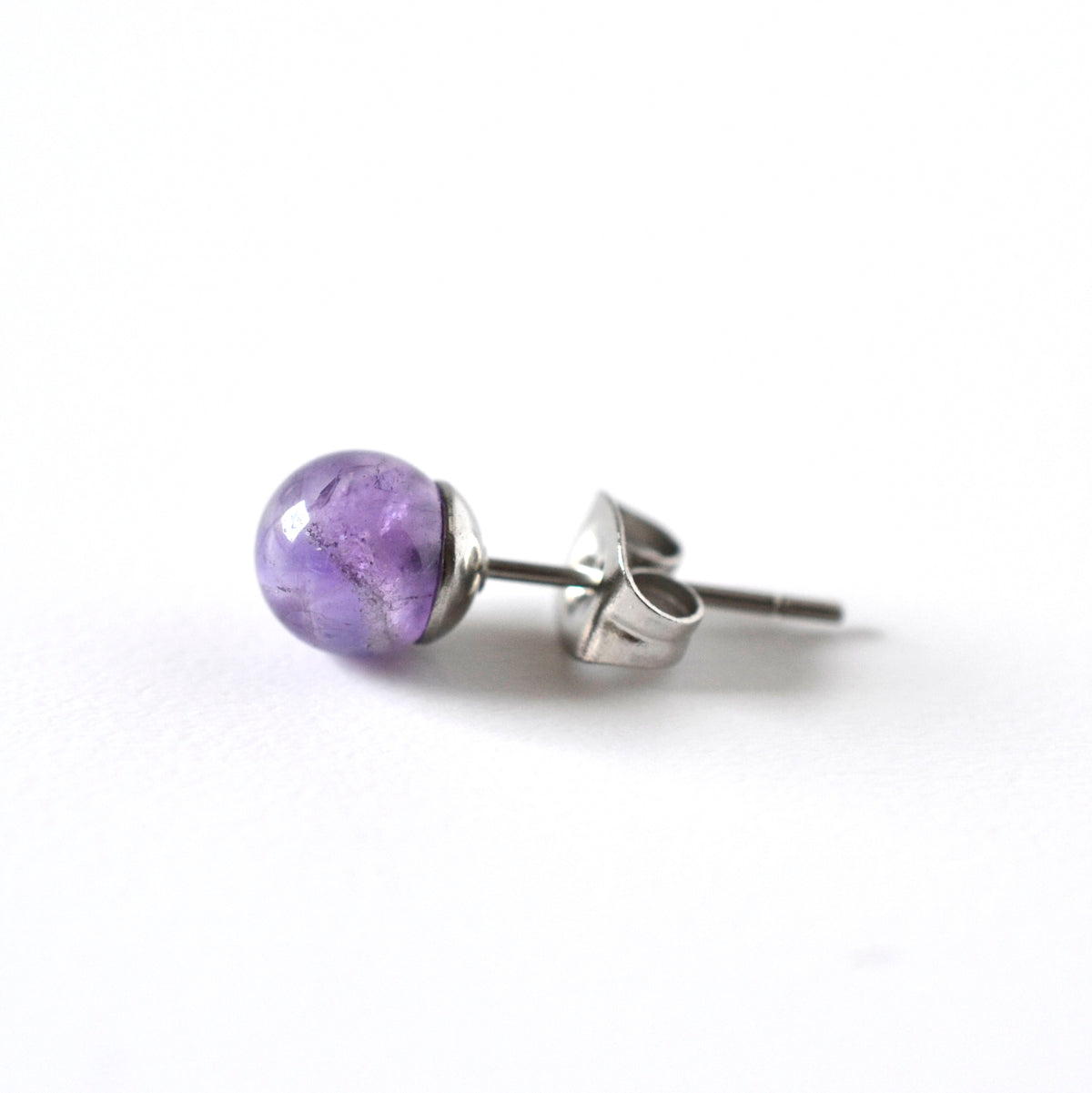A single stud earring featuring a polished purple amethyst sphere on a surgical steel setting with a butterfly back, shown on a clean white background.