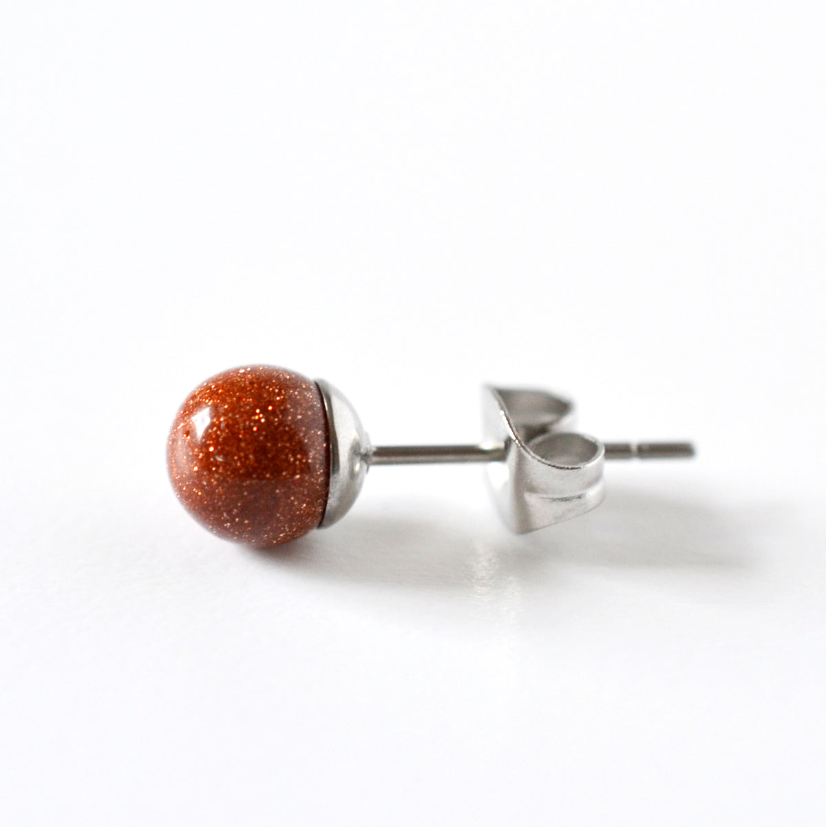A single stud earring featuring a round, polished reddish brown stone with fine gold glitter, set in surgical steel and shown from a side profile on a white background.