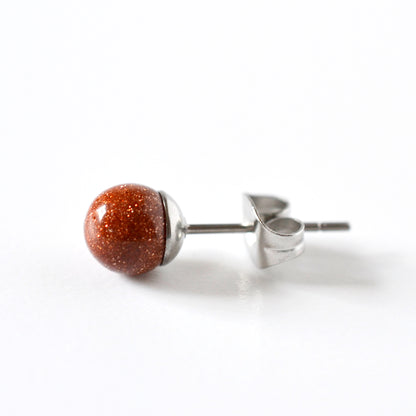 A single stud earring featuring a round, polished reddish brown stone with fine gold glitter, set in surgical steel and shown from a side profile on a white background.