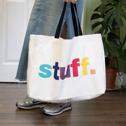 Person holding a white tote bag with colorful text 'stuff.' in an indoor setting.
