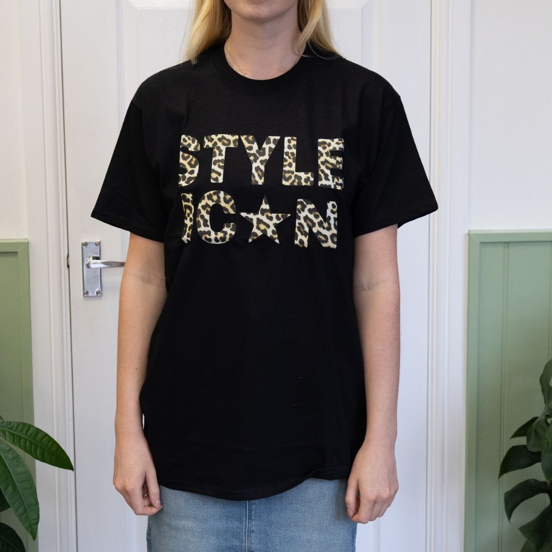 Person wearing a black t-shirt with 'STYLE ICON' text in leopard print, standing in front of a white door.