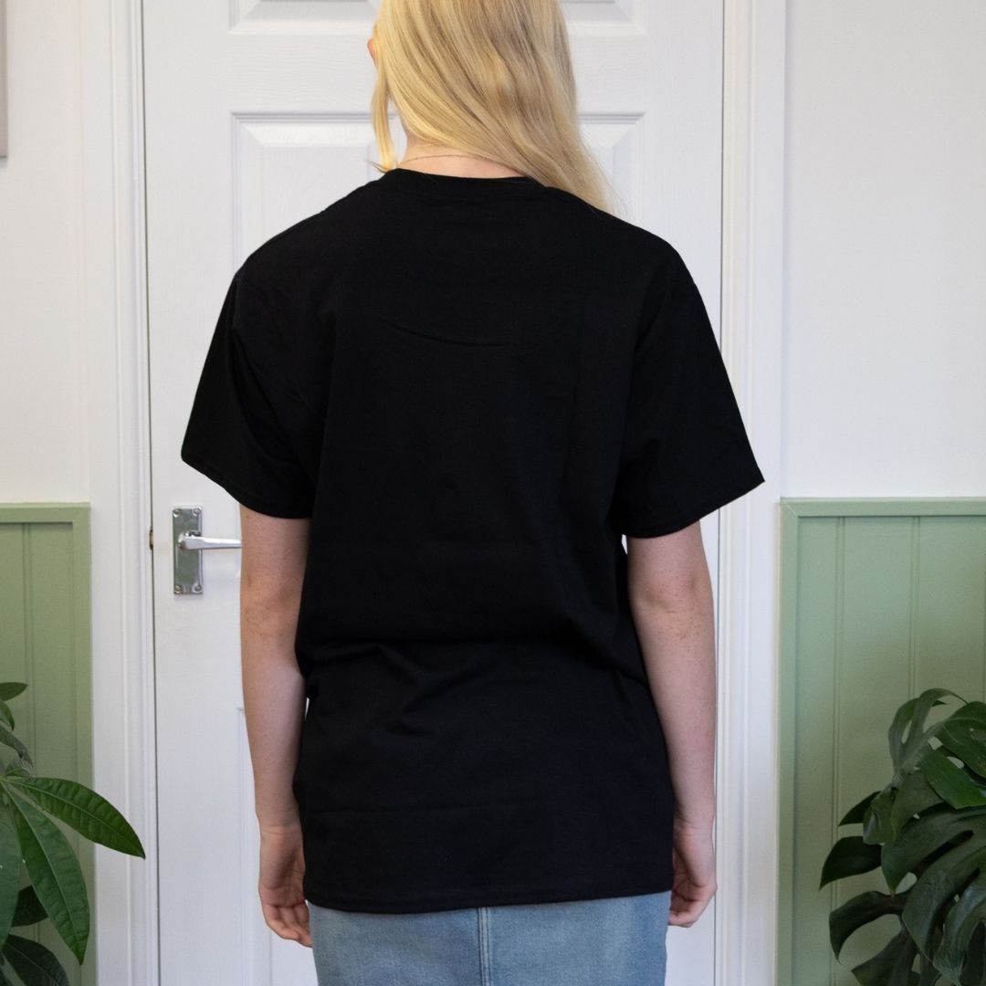Person wearing a black t-shirt facing a white door with plants on either side.