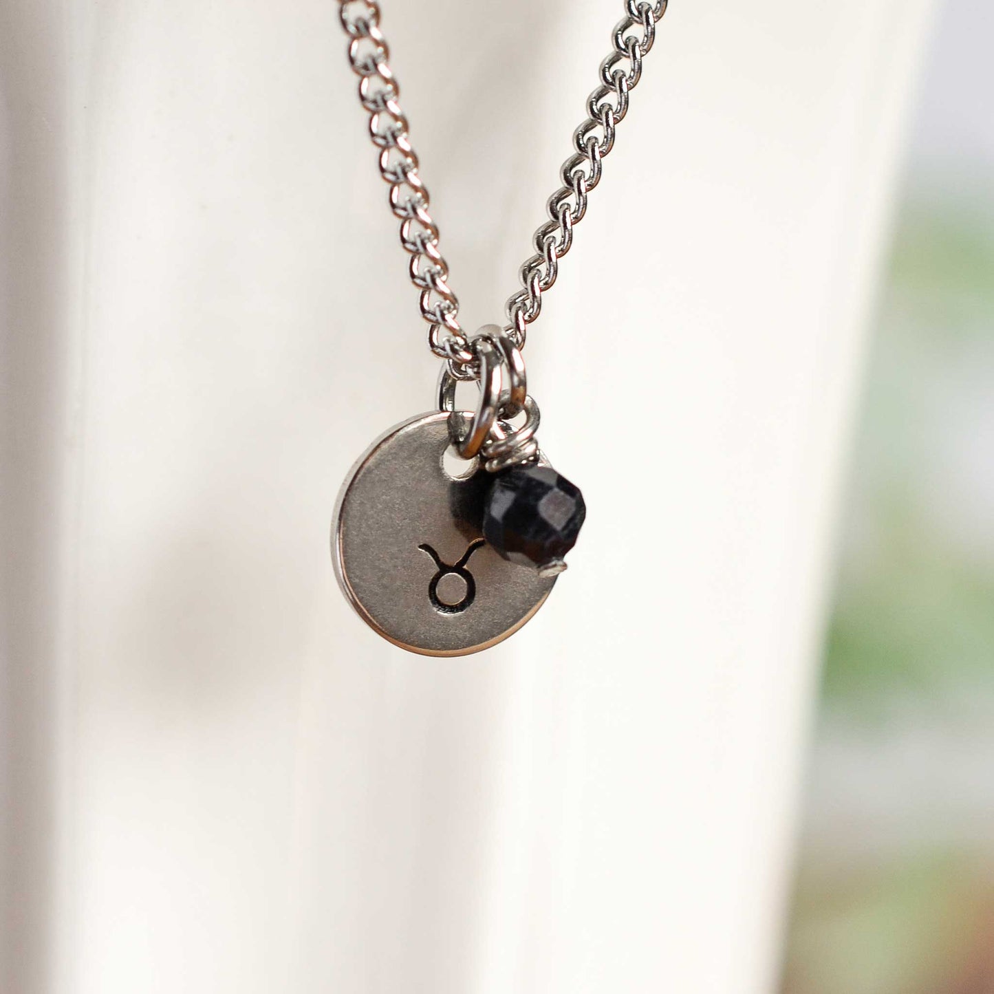 Close up of Taurus zodiac sign necklace with Sapphire gemstone charm on stainless steel chain